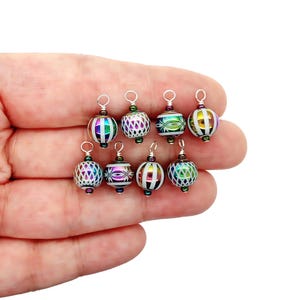 May include: A collection of nine colorful, round glass bead charms with silver-tone findings. The charms feature various patterns and colors, including stripes, geometric designs, and iridescent finishes. Each charm is approximately 0.75 inches in diameter.