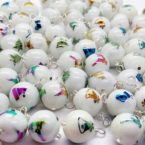 May include: A collection of white, round, Christmas ornaments with silver wire loops. Each ornament features a different iridescent design, including trees, bells, and musical notes.