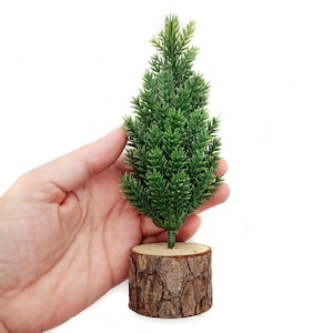 May include: A small artificial pine tree with green needles, potted in a brown bark-like material.
