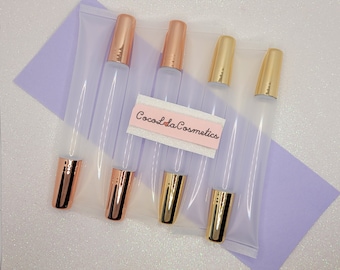 Puede incluir: Cinco tubos transparentes de brillo de labios con tapas doradas y de oro rosa. Los tubos están empaquetados en una bolsa de plástico transparente con una etiqueta rosa que dice "Coco La Cosmetics".