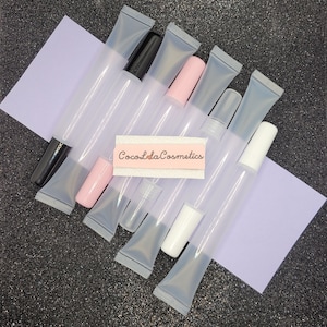 May include: A group of clear plastic tubes with different colored caps, including pink, white, and black. The tubes are arranged on a purple surface with the text "CocoIda Cosmetics" visible in the center.