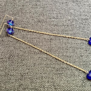 May include: A pair of long gold chain earrings with blue heart-shaped charms. The charms have a slightly iridescent finish.