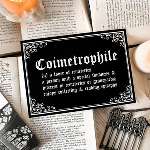 Puede incluir: Un letrero en blanco y negro con la palabra "Coimetrophile" en una fuente decorativa. El letrero define la palabra como "un amante de los cementerios, una persona con una especial afici&oacute;n e inter&eacute;s en los cementerios o los cementerios; disfruta coleccionando y leyendo epitafios."