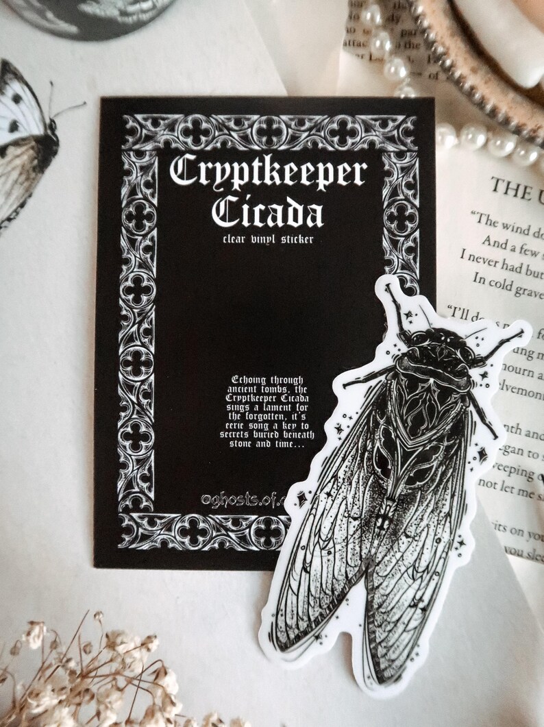 May include: A black and white clear vinyl sticker featuring a detailed illustration of a cicada insect. The sticker is next to a black card with the text "Cryptkeeper Cicada" and decorative border. The card also includes additional text.