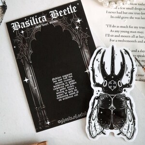 May include: Black and white sticker of a beetle with a gothic archway background. The sticker has the text "Basilica Beetle" and "Folklore suggests you may find this curious creature wandering in gothic cathedrals and hidden in gothic arches. waiting to bless a passer by with the enchanting sound of its orchestral call."
