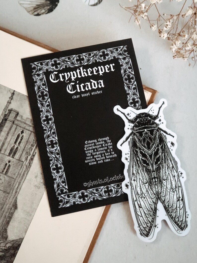 May include: A black and white clear vinyl sticker featuring a detailed cicada illustration. The sticker is next to a black card with the text "Cryptkeeper Cicada" and additional text. The design has a gothic aesthetic.