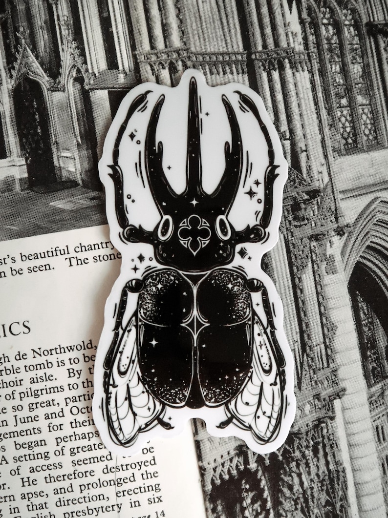 May include: Black and white sticker of a beetle with intricate details and a starry background. The beetle has large horns and wings.