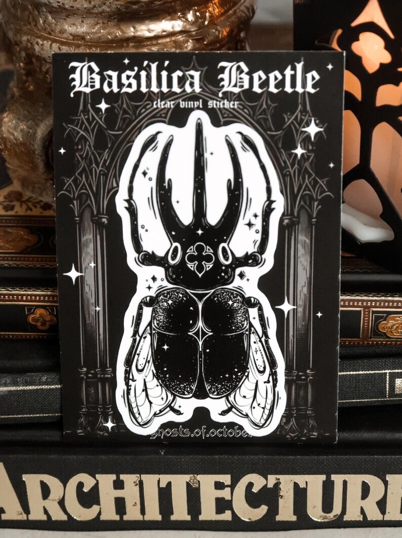 May include: Black and white sticker of a beetle with a gothic archway background. The sticker says "Basilica Beetle" and "clear vinyl sticker".