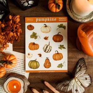 May include: A collection of fall-themed items, including pumpkin stickers, candles, and decorative pumpkins. The sticker sheet features various pumpkin illustrations with leaves. A butterfly and pencils are also present.