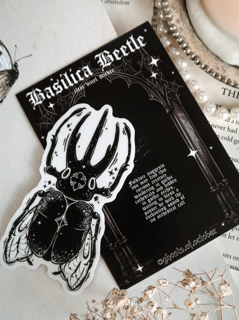May include: A black and white sticker of a beetle with intricate details. The sticker is on a black background with white text that reads "Basilica Beetle clear vinyl sticker" and "Folklore suggests you may find this curious creature wandering in gothic cathedrals and hidden in gothic arches, waiting to bless a passer by with the enchanting sound of its orchestral call" and "oghosts.of.october".