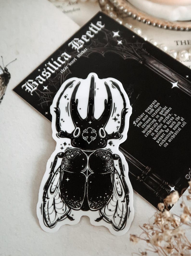 May include: Black and white sticker of a beetle with intricate details and a starry background. The sticker is labeled "Basilica Beetle" and has text about folklore and the creature's connection to gothic architecture.