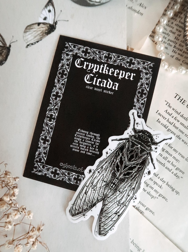 May include: A clear vinyl sticker featuring a detailed black and white illustration of a cicada insect. The sticker is labeled "Cryptkeeper Cicada" with gothic-style text on a black background. The design has a vintage, spooky aesthetic.
