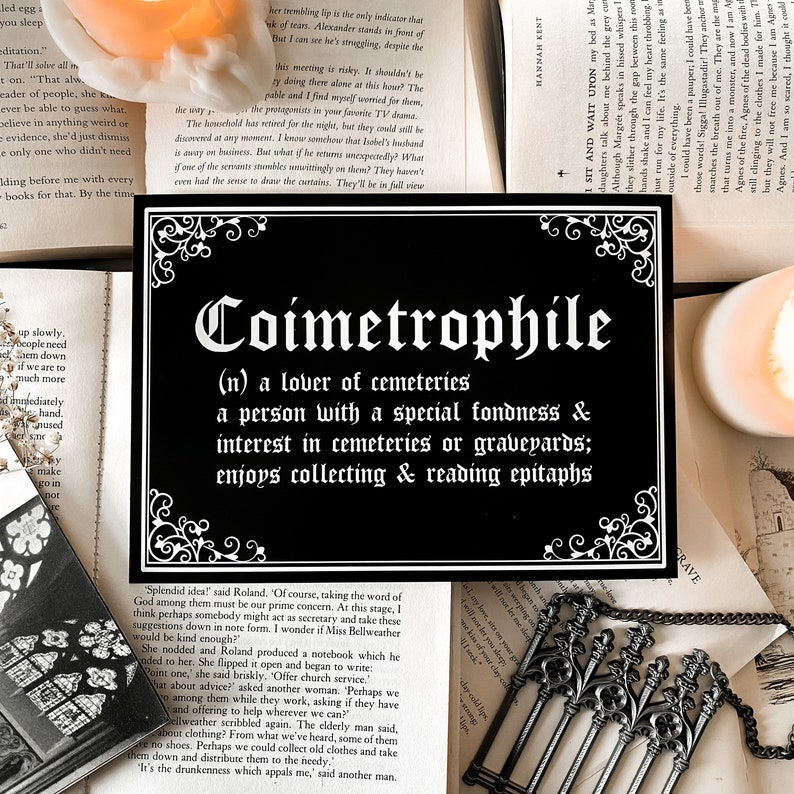 Puede incluir: Un letrero en blanco y negro con letras ornamentadas que definen la palabra "Coimetrophile" como un amante de los cementerios. El letrero tambi&eacute;n describe a un coimetrophile como una persona con una especial predilecci&oacute;n e inter&eacute;s por los cementerios o los cementerios, a quien le gusta coleccionar y leer epitafios.