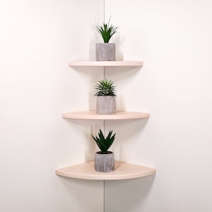 Puede incluir: Tres estantes de esquina de madera con un acabado de madera clara, cada uno con una planta suculenta en maceta. Las plantas están en macetas de hormigón gris.