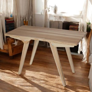 May include: A light-colored wooden desk with a rectangular top and angled legs. The desk is made of light-colored wood and has a natural finish. The legs are angled for stability. The desk is approximately 48 inches long.