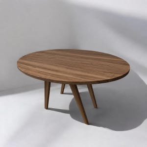 Op de afbeelding: Een ovale salontafel gemaakt van bruin hout met een zichtbaar nerfpatroon. De tafel heeft een glad, plat bovenoppervlak dat wordt ondersteund door vier schuine, taps toelopende houten poten die vanuit het midden naar de vloer uitlopen.
