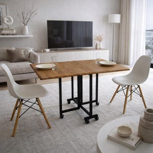 May include: A wooden folding table with a black metal frame and wheels, set for two. Two white chairs with wooden legs and black wire supports are positioned on either side. The table is approximately 91 cm long.