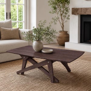 May include: A dark brown wooden coffee table with a rectangular top and a crisscross leg base. A light-colored ceramic vase containing green leafy branches and a small, shallow, round ceramic bowl are placed on the surface of the table.