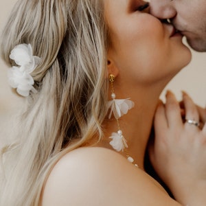 May include: A close-up of a bride and groom kissing. The bride is wearing a white flower in her hair and long, delicate white flower earrings.