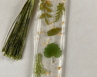 May include: A green tassel bookmark with pressed leaves and gold flakes embedded in clear resin.