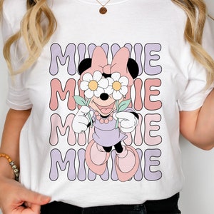 May include: White t-shirt with a graphic of Minnie Mouse wearing flowers over her eyes. The text "MINNIE" is repeated four times in a retro font.