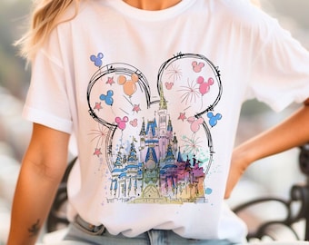 Può includere: Maglietta bianca con un'illustrazione colorata del castello di Cenerentola con le orecchie di Topolino e palloncini. Il castello è circondato da fuochi d'artificio.