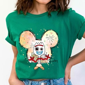 May include: Green t-shirt with a cartoon drawing of Forky from Toy Story. Forky is standing inside a Mickey Mouse head outline with a colorful background. The text "Forky" is written below the image.