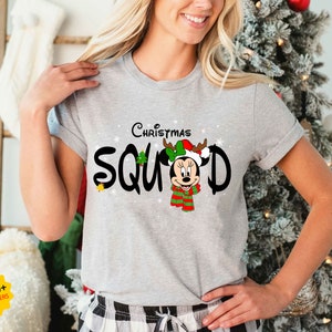 May include: Gray t-shirt with a Christmas-themed design featuring Mickey Mouse wearing a Santa hat and reindeer antlers. The text "Christmas Squad" is printed in black with a white outline.
