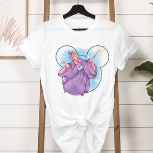 May include: White t-shirt with a purple and blue illustration of a fairy godmother holding a wand inside a Mickey Mouse head silhouette.