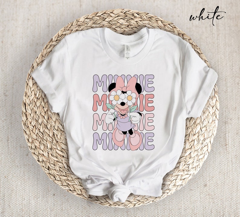 May include: White t-shirt with a graphic of Minnie Mouse wearing flowers over her eyes. The text "MINNIE" is repeated four times in a wavy font.