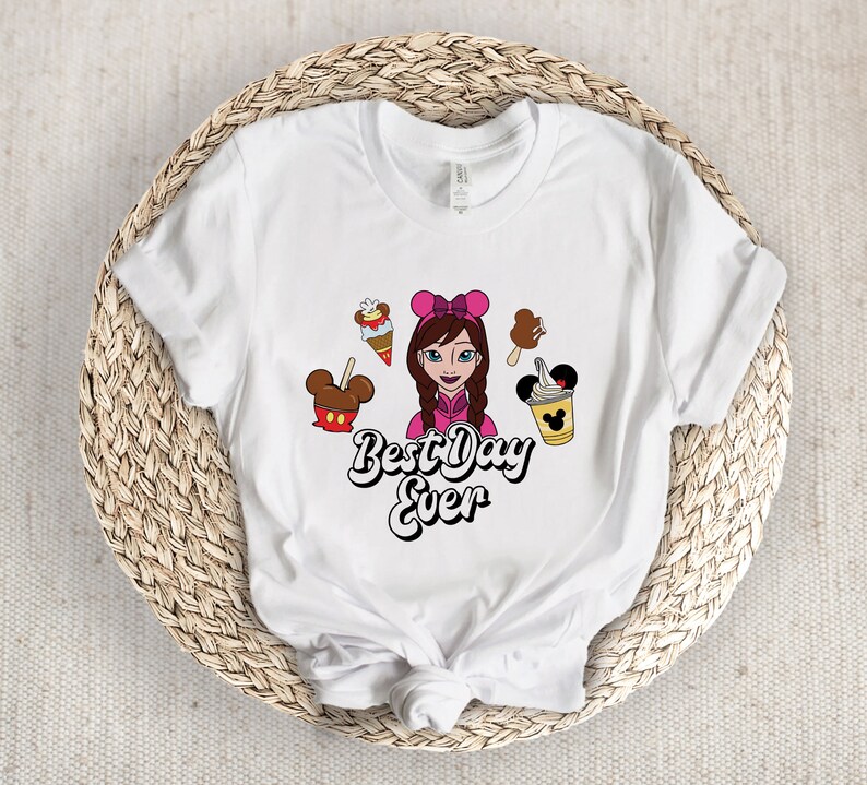 May include: White t-shirt with a cartoon design of a girl with a pink bow and treats. The words "Best Day Ever" are in a fun font. The design includes ice cream, Mickey Mouse-shaped treats, and a drink, perfect for a fun day out.