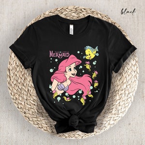 Peut inclure: T-shirt noir avec un motif d'Ariel de La Petite Sir&egrave;ne. Le motif repr&eacute;sente Ariel nageant avec un poisson jaune et des hippocampes. Le texte "The Little Mermaid" est imprim&eacute; au-dessus d'Ariel.