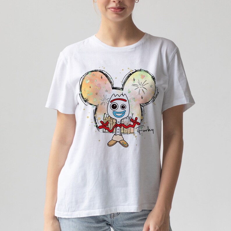 May include: White t-shirt with a colorful illustration of Forky from Toy Story. The illustration is inside a Mickey Mouse head silhouette with fireworks and a castle in the background. The text "Forky" is written below the illustration.