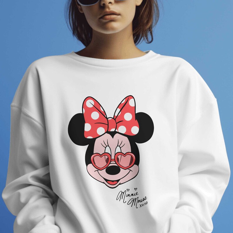 May include: White sweatshirt with a Minnie Mouse graphic. The design shows Minnie wearing heart-shaped sunglasses and a red polka dot bow. The text "Minnie Mouse xoxo" is in a script font. The background is blue.