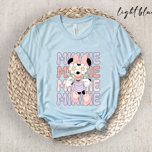 May include: Light blue t-shirt with a graphic of Minnie Mouse wearing flowers over her eyes. The text "MINNIE" is repeated four times in a retro font.