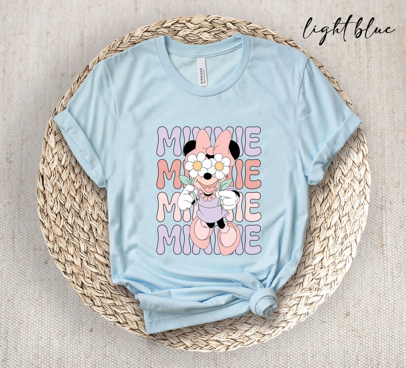 May include: Light blue t-shirt with a graphic of Minnie Mouse wearing flowers over her eyes. The text "MINNIE" is repeated four times in a retro font.