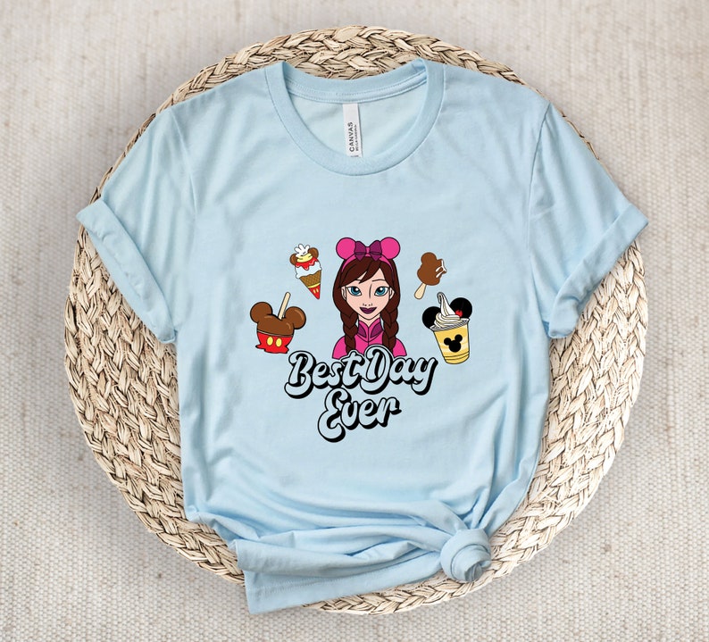 May include: Pale blue t-shirt featuring a cartoon girl, ice cream, and the text "Best Day Ever". The shirt is made of a soft material and has rolled-up sleeves. The graphic includes a Mickey Mouse ice cream bar.