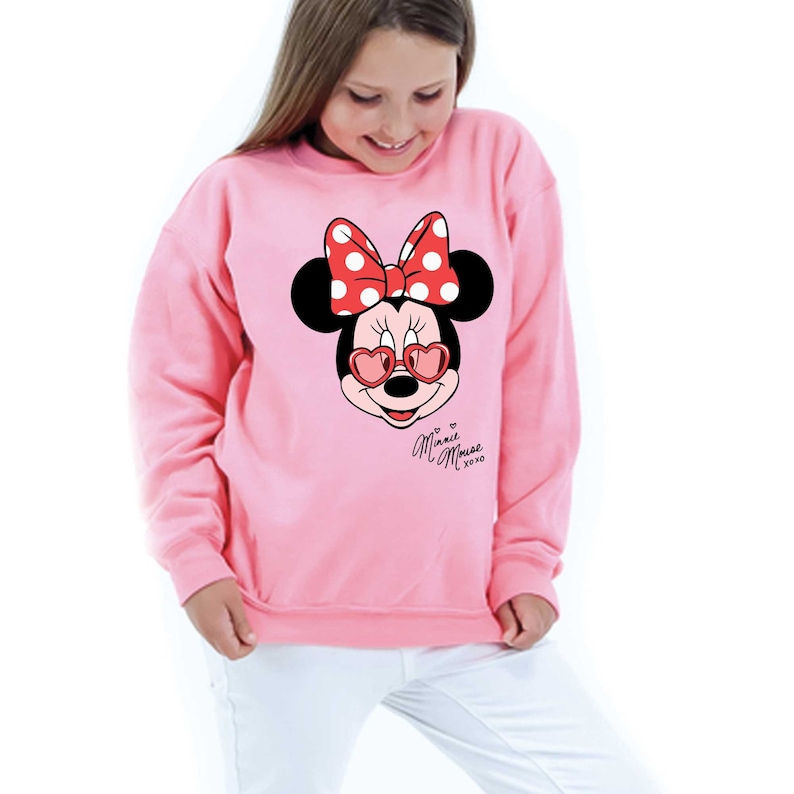 May include: Pale pink sweatshirt with a Minnie Mouse design. The design shows Minnie's face wearing heart-shaped sunglasses and a red polka dot bow. The text "Minnie Mouse xoxo" is below the graphic.