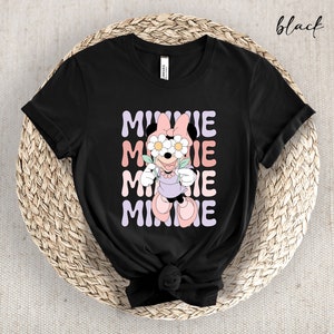 May include: Black t-shirt with a graphic of Minnie Mouse wearing flowers over her eyes. The text "MINNIE" is repeated in a stacked pattern in pastel colors.