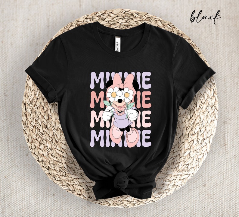 May include: Black t-shirt with a graphic of Minnie Mouse wearing flowers over her eyes. The text "MINNIE" is repeated in a stacked pattern in pastel colors.