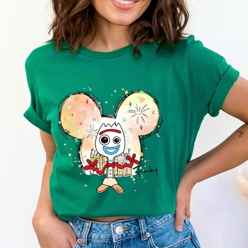 May include: Green t-shirt with a cartoon drawing of Forky from Toy Story. Forky is standing inside a Mickey Mouse head outline with a colorful background. The text "Forky" is written below the image.