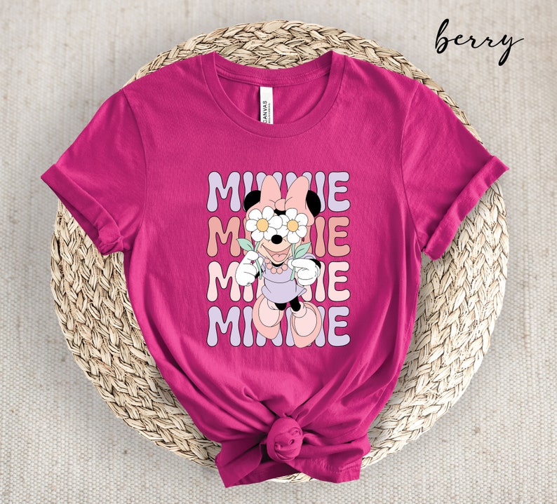 May include: A pink t-shirt with a graphic of Minnie Mouse wearing flowers over her eyes. The text "MINNIE" is repeated four times in a retro font.