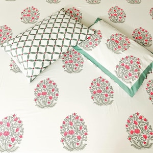 K&ouml;nnte beinhalten: Wei&szlig;es Bettw&auml;sche-Set mit einem floralen Muster in Rosa und Grau. Ein Kissenbezug hat ein gr&uuml;n-wei&szlig;es geometrisches Design. Der andere hat einen gr&uuml;nen Rand.