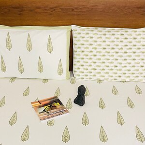 May include: White bed linen with a green leaf pattern. A book and a small statue are on the bed.