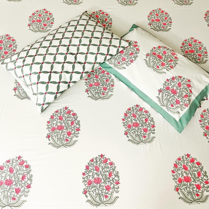 K&ouml;nnte beinhalten: Wei&szlig;es Bettw&auml;sche-Set mit einem floralen Muster in Rosa und Grau. Ein Kissenbezug hat ein gr&uuml;n-wei&szlig;es geometrisches Design. Der andere hat einen gr&uuml;nen Rand.