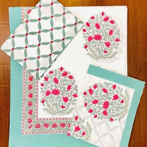 K&ouml;nnte beinhalten: Ein Set aus wei&szlig;em und t&uuml;rkisfarbenem Tischw&auml;sche mit Blumendruck. Das Set umfasst eine Tischdecke, Servietten und Tischsets. Die Tischdecke und die Tischsets weisen ein gro&szlig;es Blumendesign in Rot und Gr&uuml;n auf. Die Servietten haben ein kleineres, sich wiederholendes Muster.