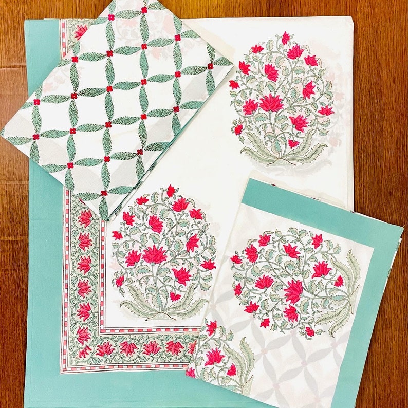 K&ouml;nnte beinhalten: Ein Set aus wei&szlig;em und t&uuml;rkisfarbenem Tischw&auml;sche mit Blumendruck. Das Set umfasst eine Tischdecke, Servietten und Tischsets. Die Tischdecke und die Tischsets weisen ein gro&szlig;es Blumendesign in Rot und Gr&uuml;n auf. Die Servietten haben ein kleineres, sich wiederholendes Muster.