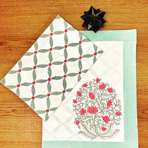 K&ouml;nnte beinhalten: Ein Geschenkset mit gemustertem Geschenkpapier und einer Karte. Das Geschenkpapier hat einen wei&szlig;en Hintergrund mit einem gr&uuml;nen und roten Blattmuster. Die Karte hat ein Blumenmuster mit roten Bl&uuml;ten und gr&uuml;nen Bl&auml;ttern. Eine schwarze Schleife liegt obenauf.