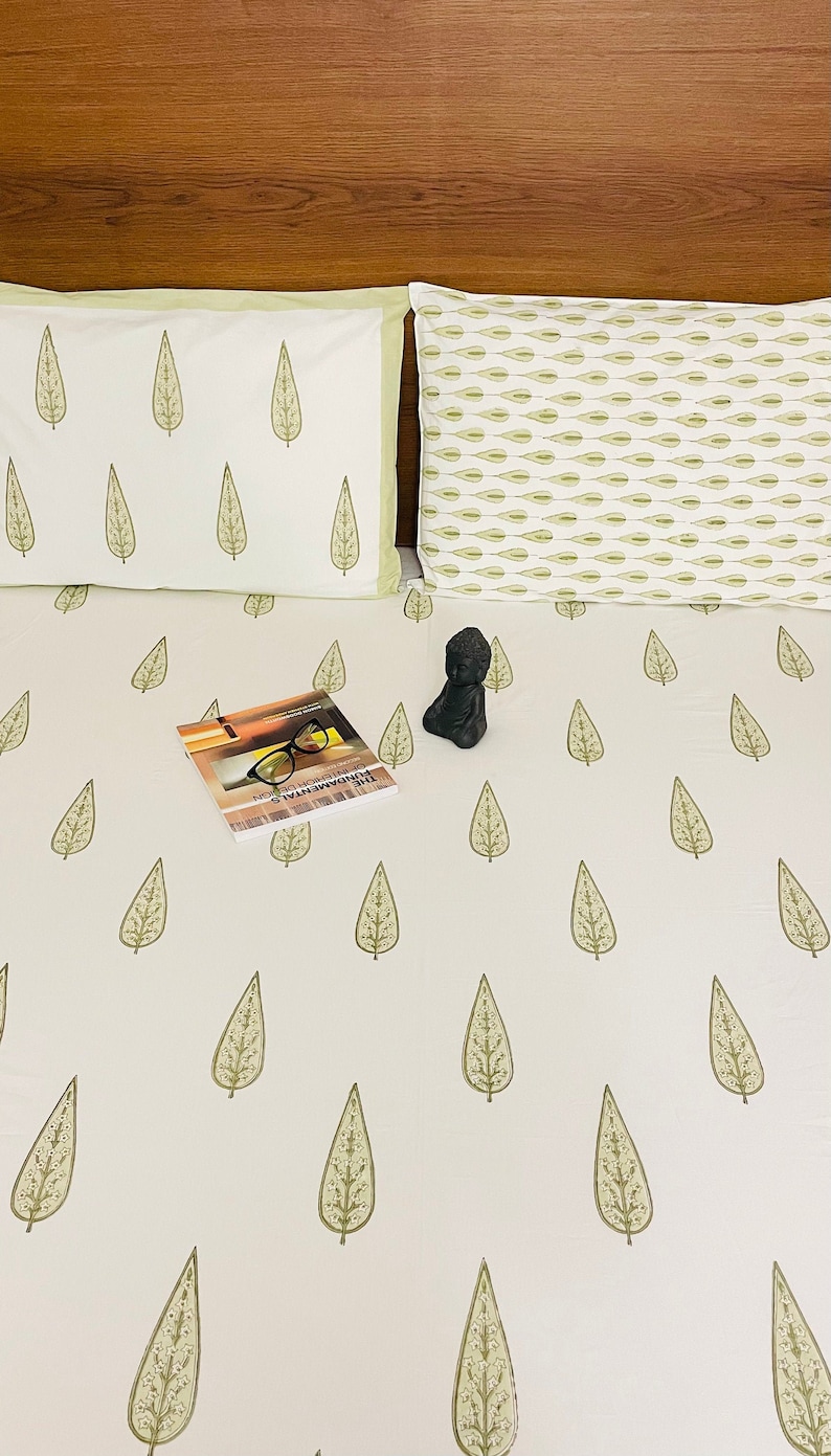 May include: White bed linen with a green leaf pattern. A book and a small statue are on the bed.