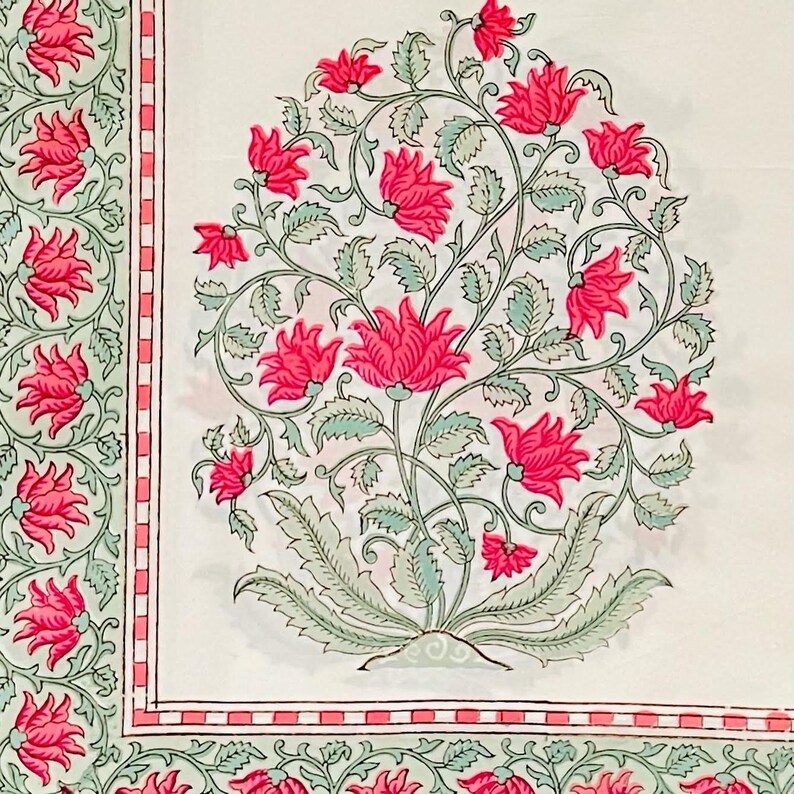 K&ouml;nnte beinhalten: Wei&szlig;er Stoff mit floralem Muster. Das Design zeigt gro&szlig;e, leuchtend rosa Bl&uuml;ten mit gr&uuml;nen Bl&auml;ttern und Stielen. Ein Rand mit einem &auml;hnlichen Blumenmotiv und einem rosa und rot gestreiften Akzent umrahmt das Hauptdesign.